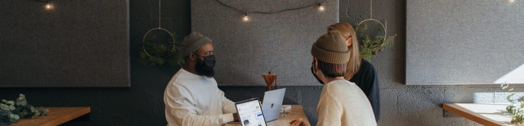 Three people surrounding a table at work wearing masks on their Surface laptops